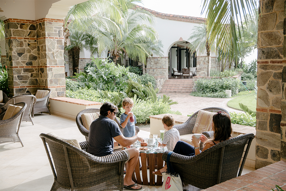 A family enjoying a meal on an outdoor terrace at Rancho Santana, highlighting the luxury and comfort of family rentals amidst lush greenery and Mediterranean-style architecture.