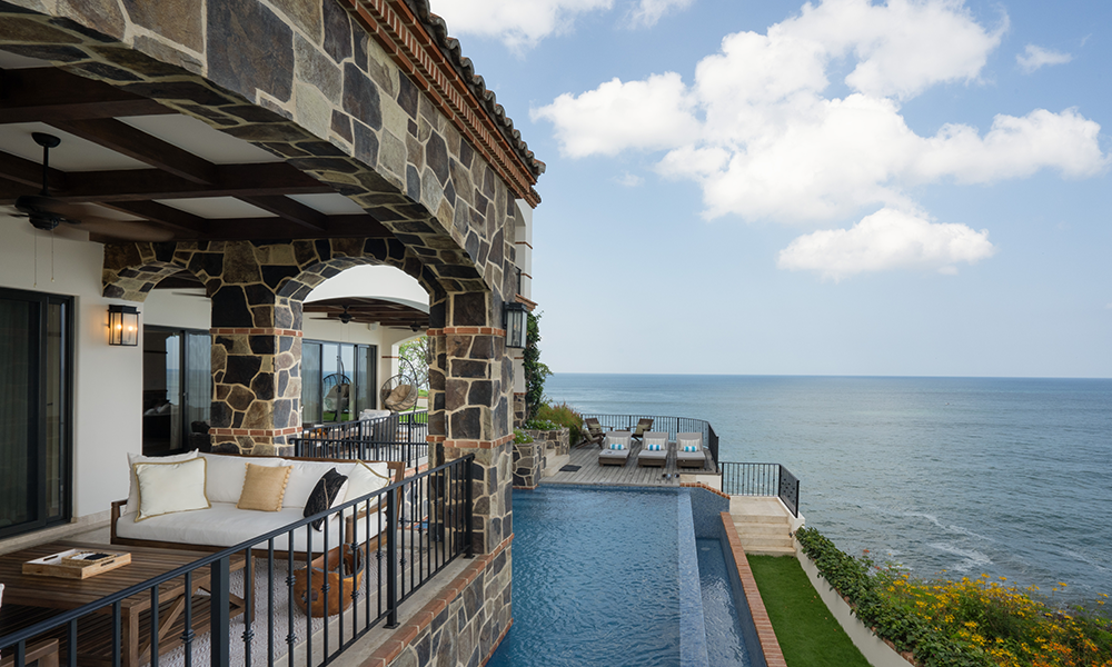 Luxury villa at Rancho Santana featuring a stone-arched terrace, infinity pool, and panoramic ocean views under a bright blue sky.