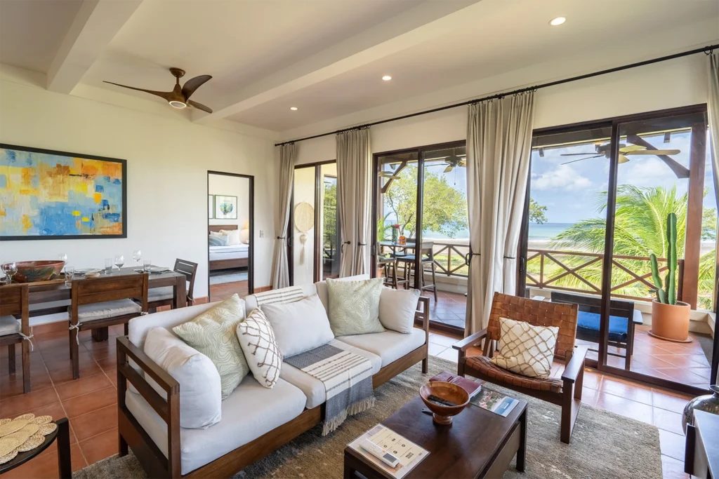 Relaxing living room in Puerta del Mar Villa 4D at Rancho Santana, featuring a plush sofa with decorative pillows, a woven accent chair, and sliding glass doors opening to a terrace with ocean views, creating a tranquil beachside ambiance.