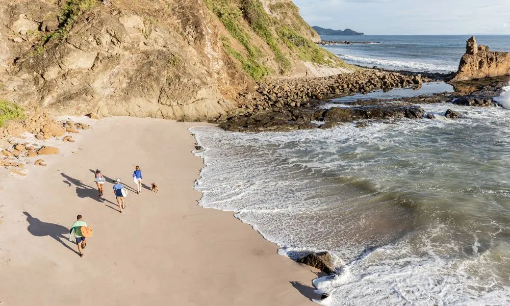 A scenic beach in Nicaragua with travelers walking along the shore near rocky cliffs, highlighting the country as a perfect destination for travel in 2025.